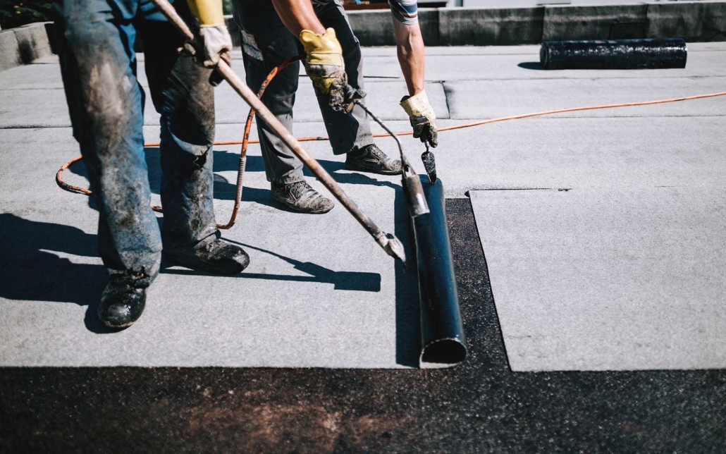 Two roofers applying a layer of asphalt roofing