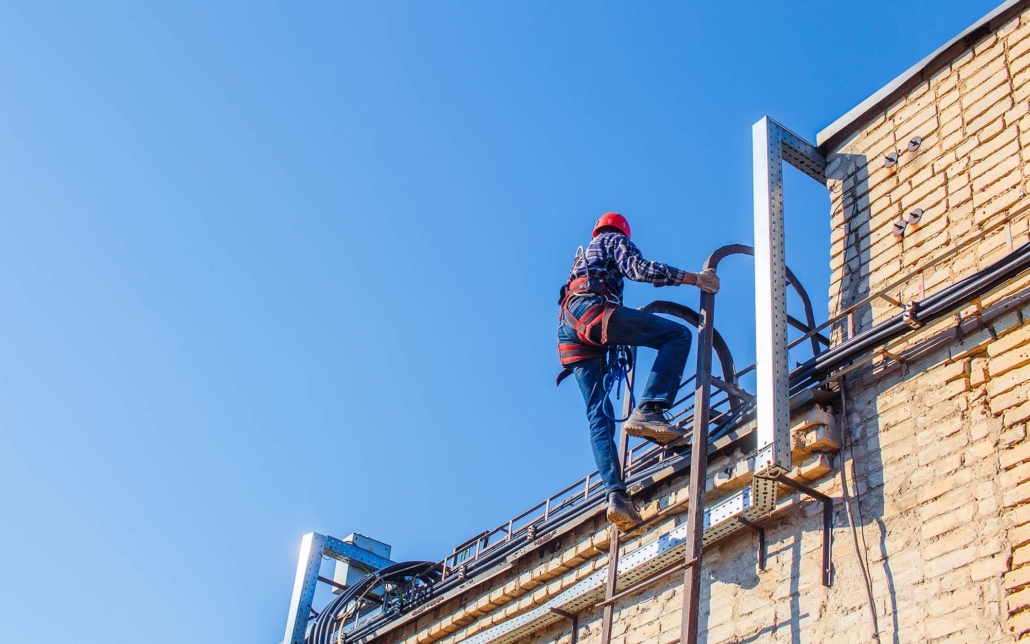 View of a roofing worker climbing ladder to commercial roof